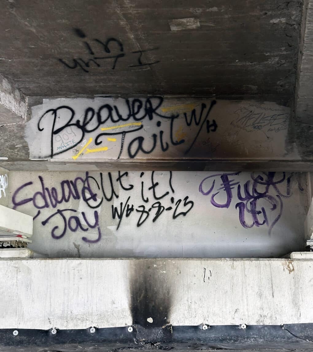 Color photograph of graffiti, in black spraypaint on concrete wall, reading "Beaver Tail" and Fuck U."