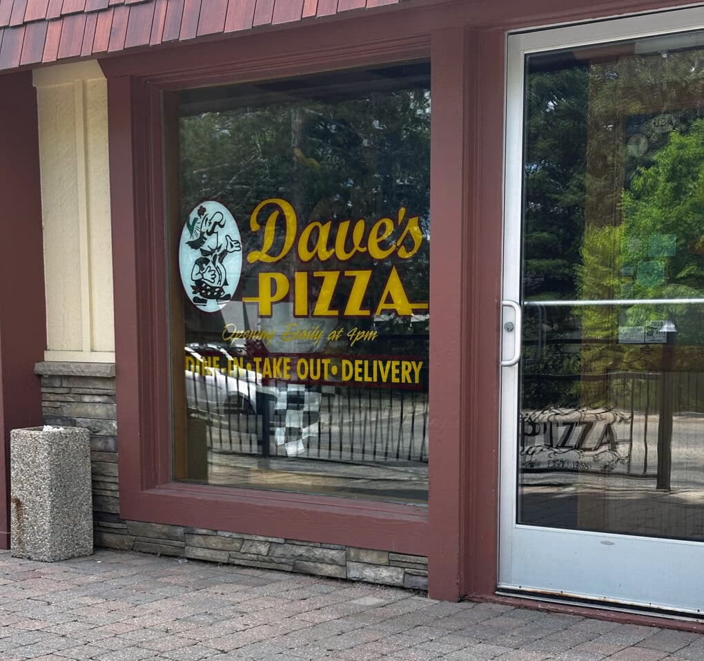Color photograph of storefront with painted sign on plate-glass window reading "Dave's Pizza."