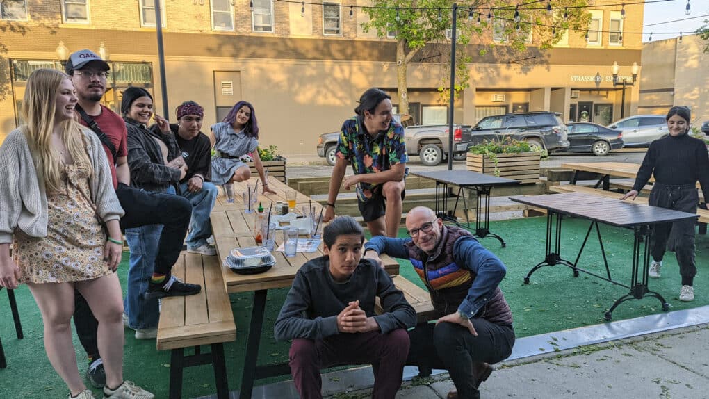 A family group of mostly young people smiling and laughing at picnic tables at an outdoor cafe.