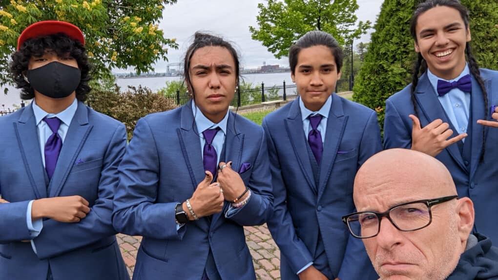Color photograph of four young men, all apparently Native American, wearing matching blue blazers, blue button-down shirts, and blue neckties, with middle-aged apparently white man.
