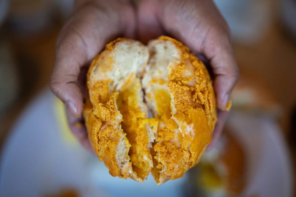 Bread-like bun with filling being broken in half.