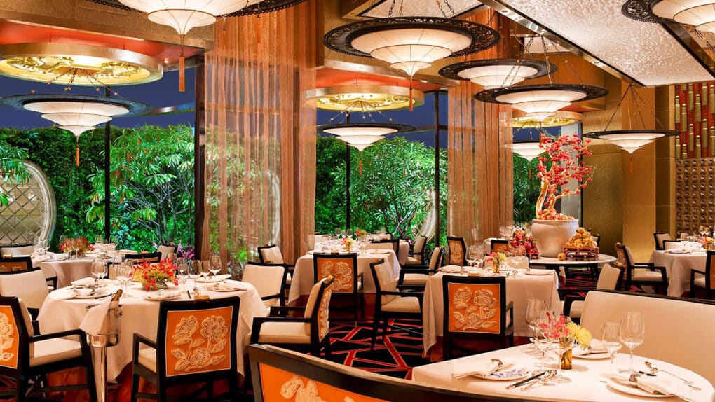 Opulent dining room with elegant lighting fixtures, ivory-inset chairs, black and red carpets.