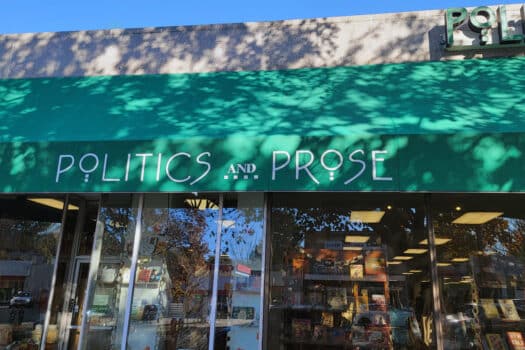 Color photograph of bookstore window with green awning, on which is written in white letters: POLITICS AND PROSE.