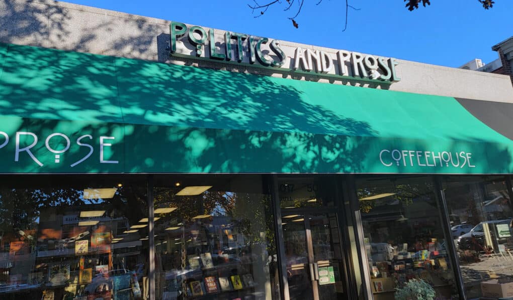 Color photograph of bookstore window with green awning, on which is written in white letters: POLITICS AND PROSE.