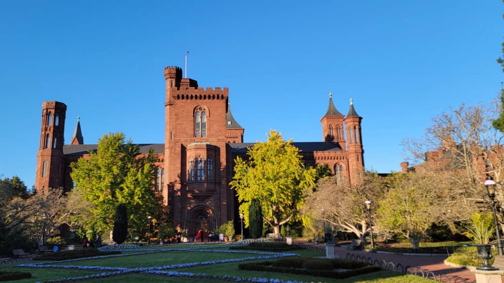 Color photograph of red-brick turretted building against bright blue sky.