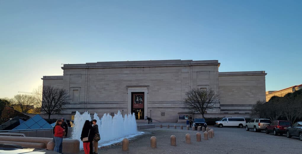 Color photograph of neoclassical museum building at dusk; a fountain in the foreground.