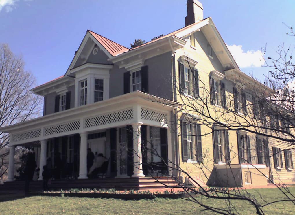 Color phtograph of large yellow brick house with deep porch and gables.