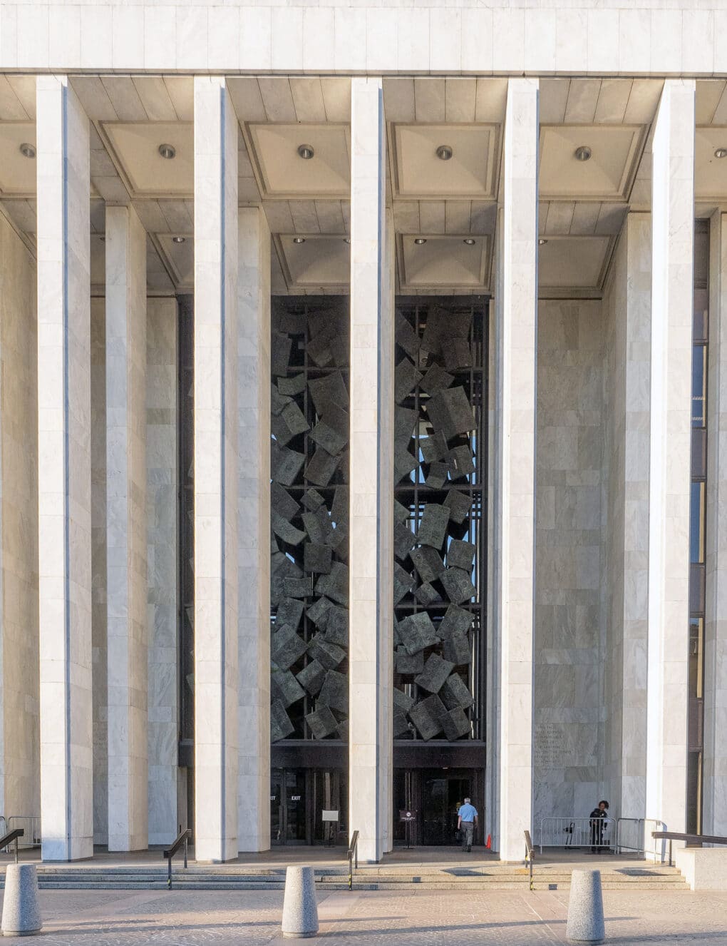 Color photograph of building entrance with tall white marble columns and abstract grid-like metal sculpture.
