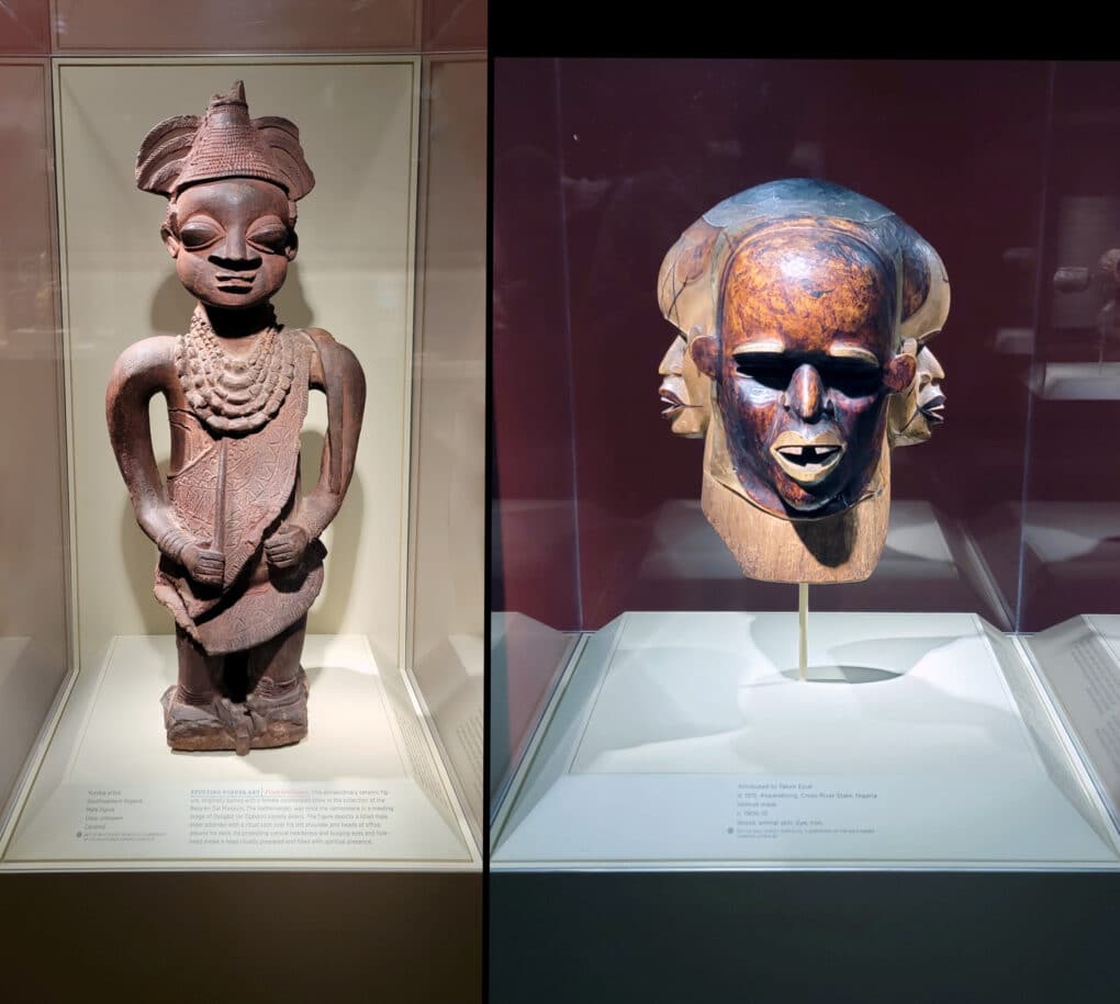 Color photographic diptych of two African sculptures in museum vitrines--one a Benin bronz figure, and one a triple-headed wooden mask.