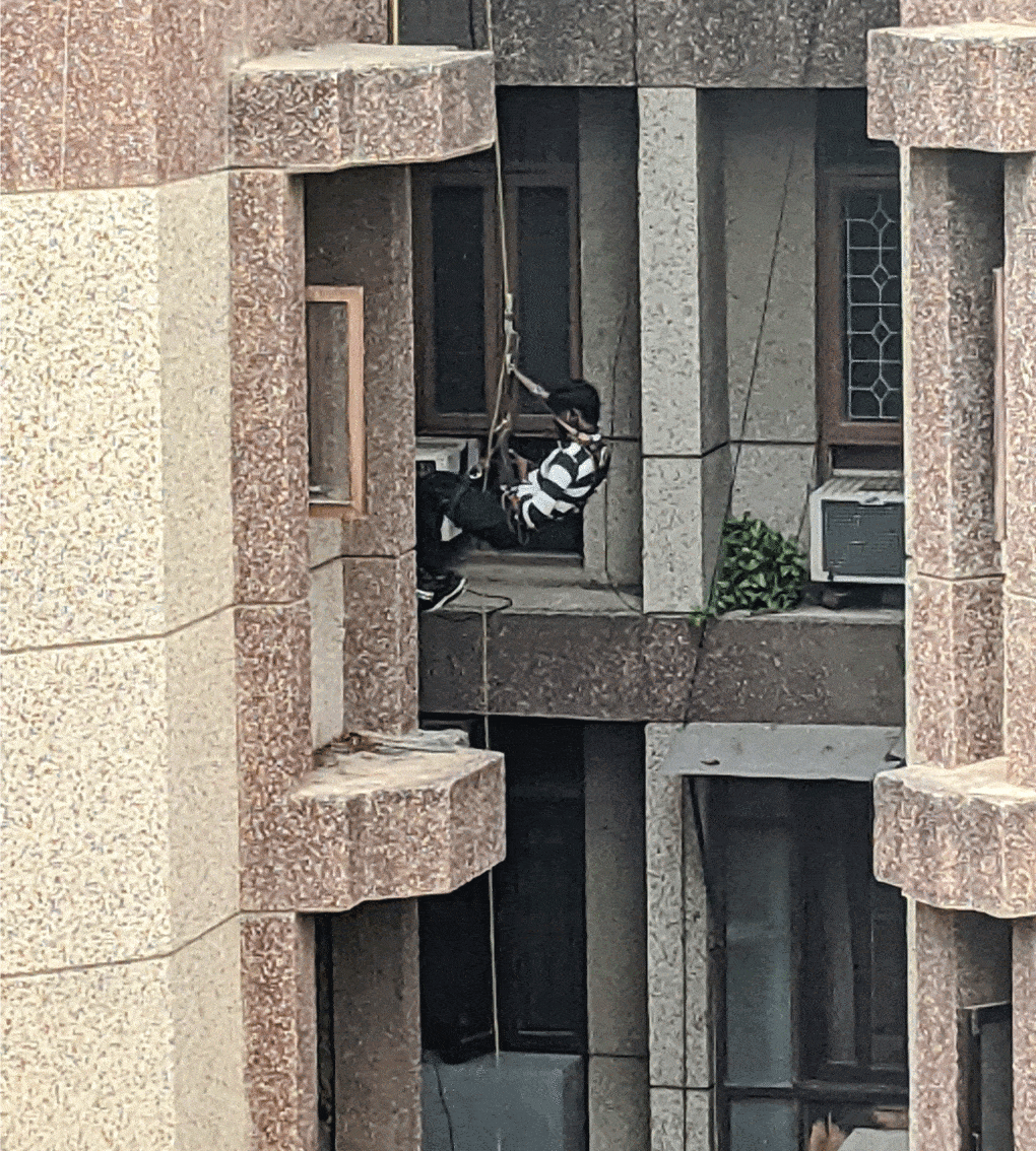 In New Delhi, India, a worker hangs precariously from a Bosun’s chair to clean an air conditioner in a residential high-rise, 2021.