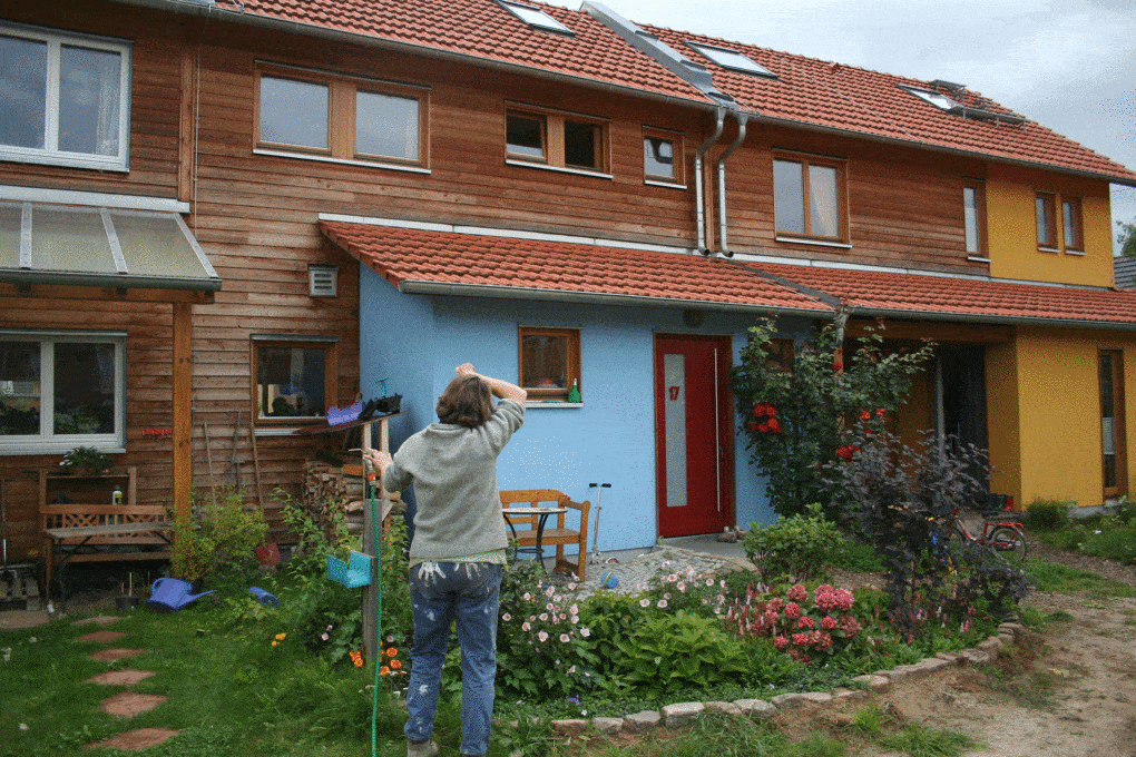 A resident of a self-built eco-village stands near Berlin stands outside a residence with a garden, 2010. 