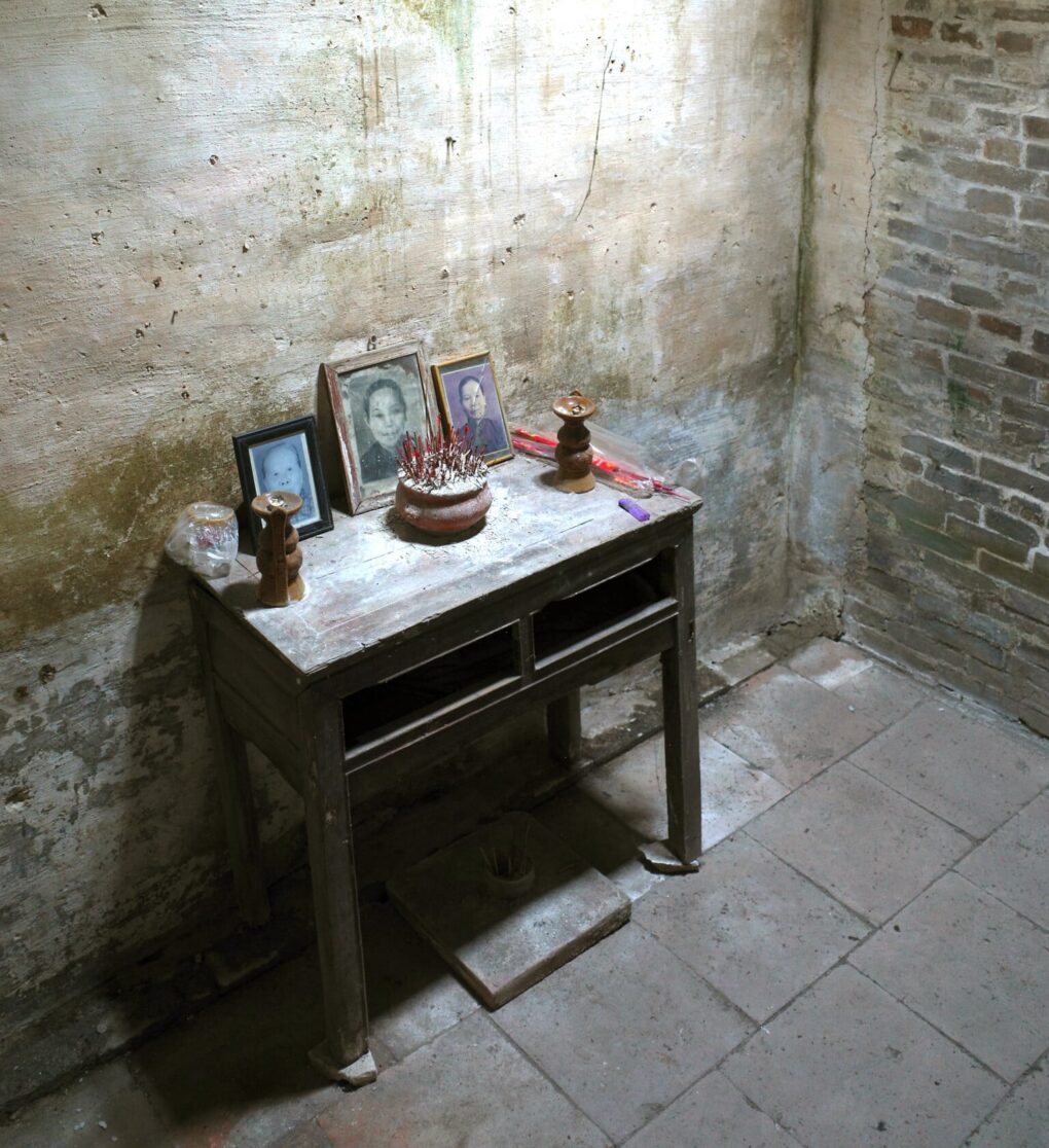 Small table with three portraits and bowl of incense stubs.