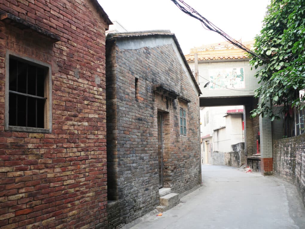 A simple brick building with a small window, photographed off a narrow street or alley.