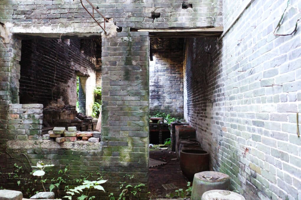 Vacant, dilapidated building being overtaken by weeds, with evidence of smoke stains on the brick.