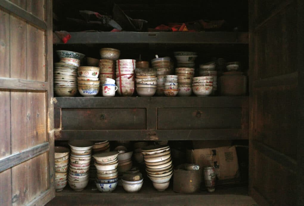 An old wooden closet filed with stacks of bowls and cups, white with floral patterns.
