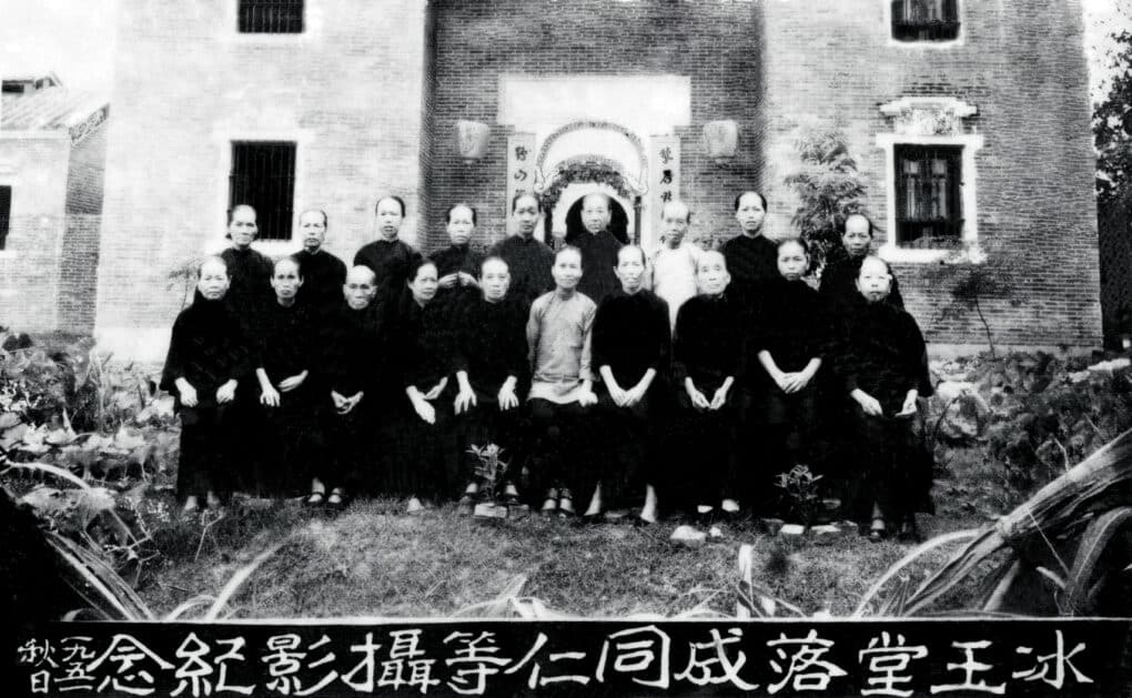 Black and white group photo of about 20 women in front of a large building, with Chinese lettering along the bottom border of the image.