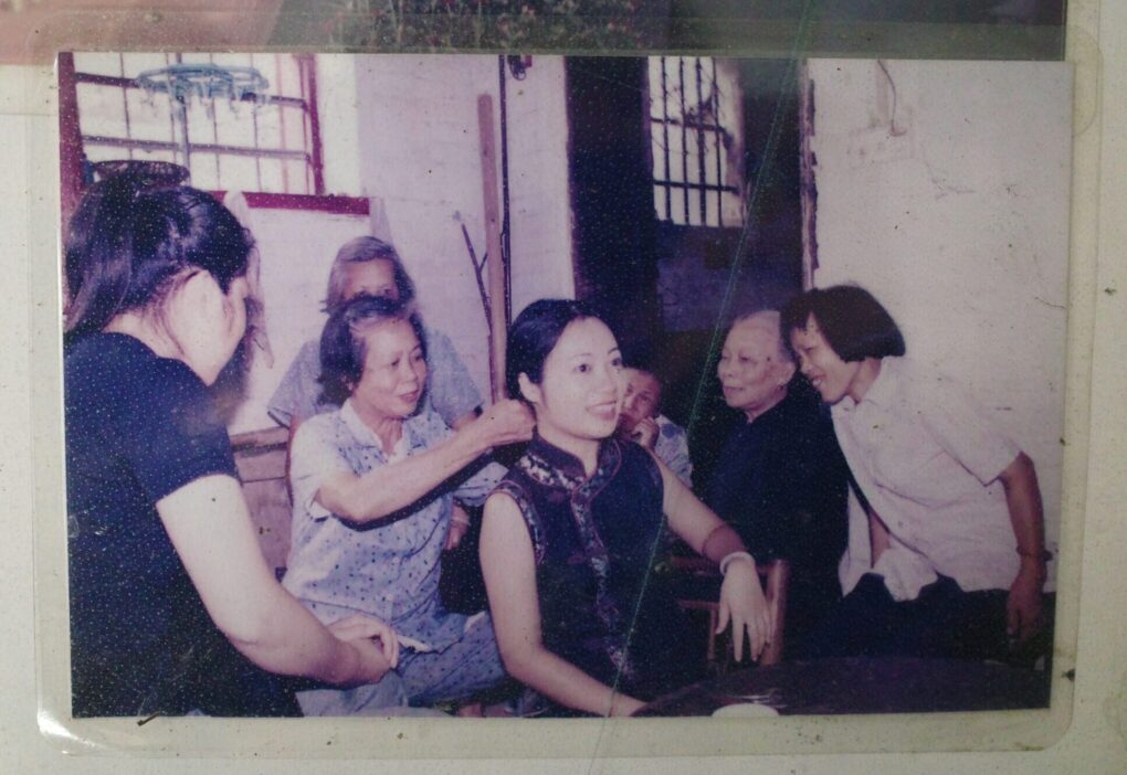 An older woman is styling a younger woman's hair, while other women eagerly look on; photo has apparently been laminated and taped to a wall.