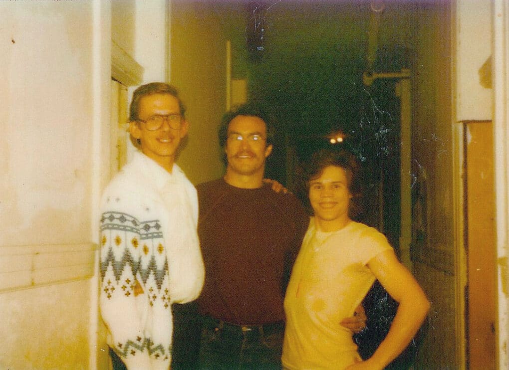 Vintage color photo of three people, smiling broadly, in a hallway. 