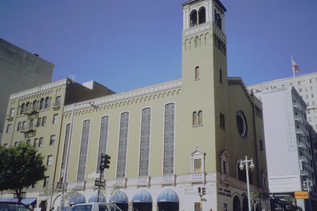 Large beige church with three-story stained class windows and a bell tower. 