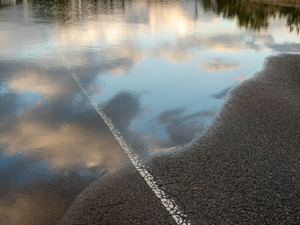 Color photograph of flooded road, with whit center line disappearing into water.