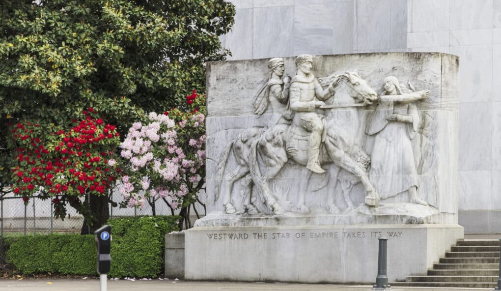 Large marble relief sculpture with two figures on a horse and one woman pointing. Bottom inscription reads, "Westward the star of empire takes its way."