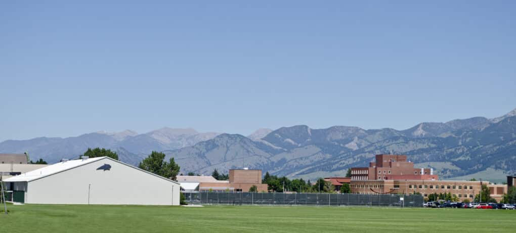 Landscape view of college grounds and agricultural fields with mountains in the background. Sky is very clear and blue.