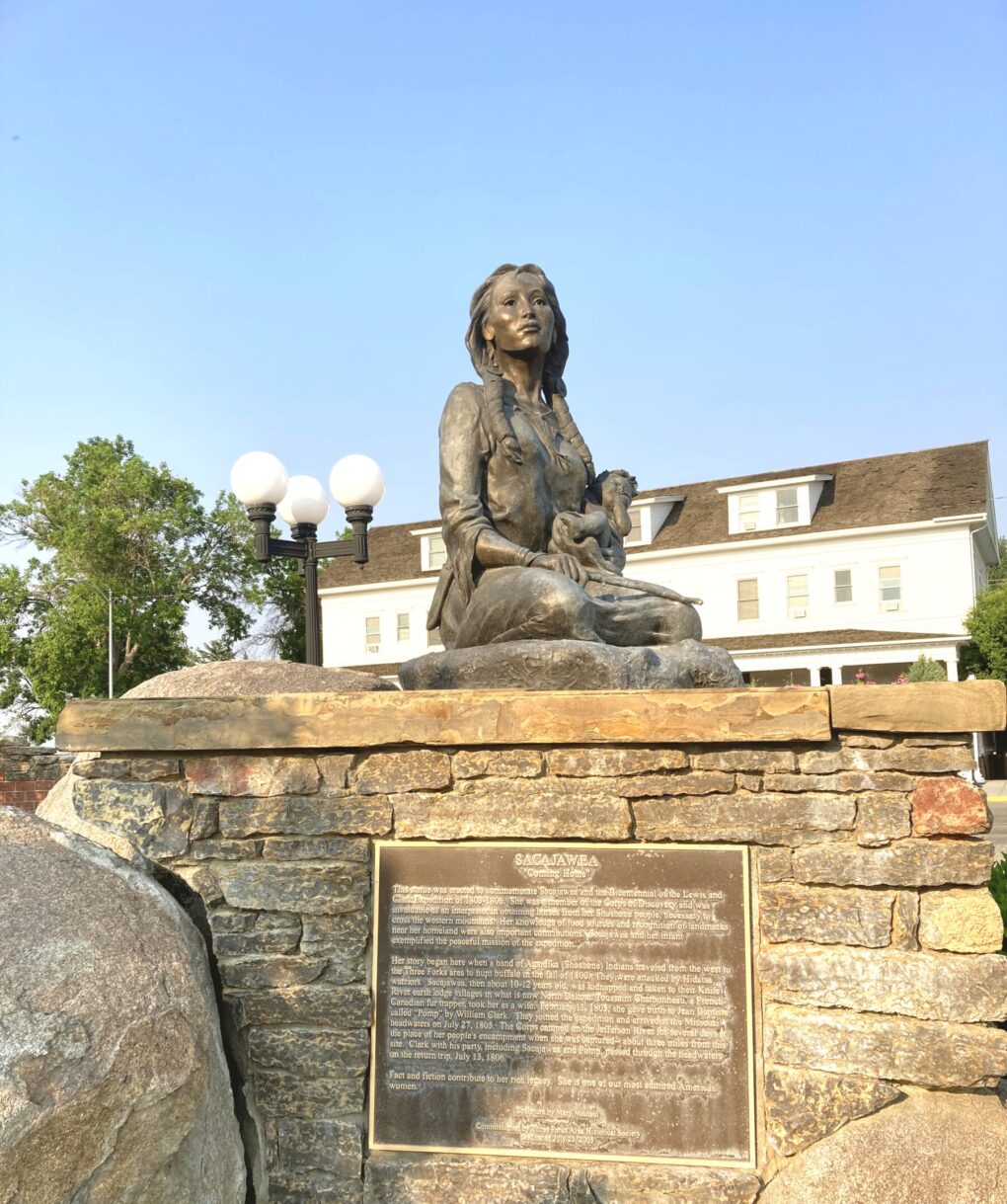 Bronze statue of woman with braids kneeling, holding an infant in her lap, gazing into distance.