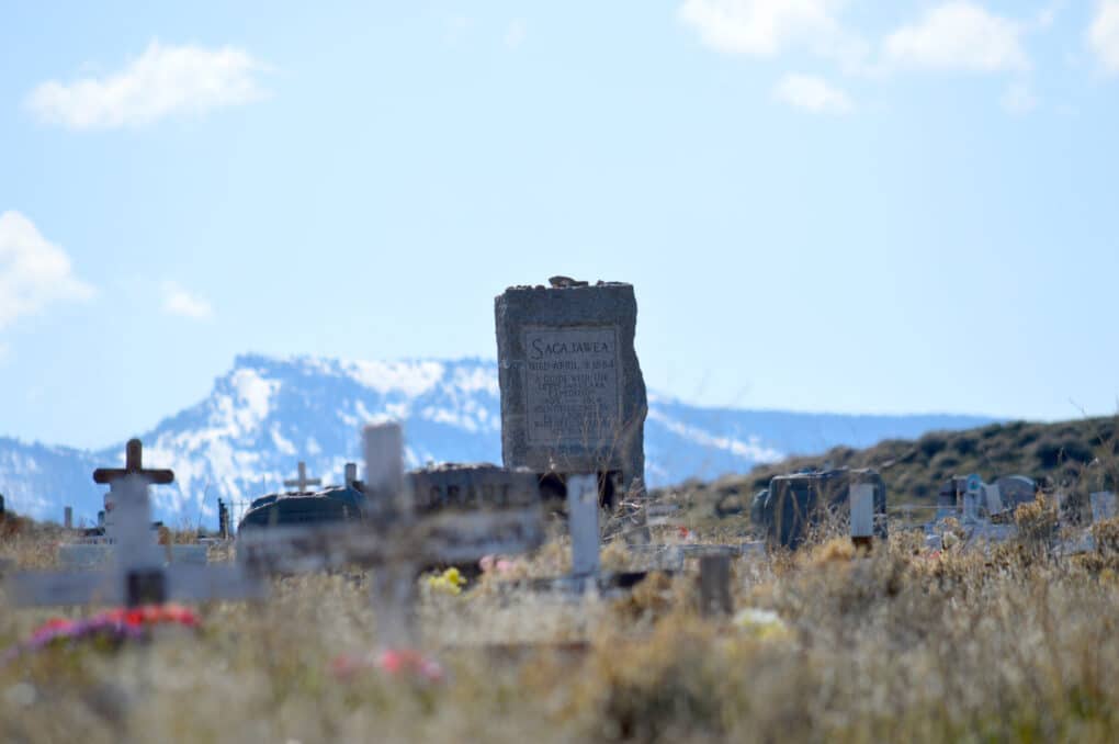 View of cemetery with snow-covered mountains in distance, and Sacajawea's prominent granite grave marker in the foreground.