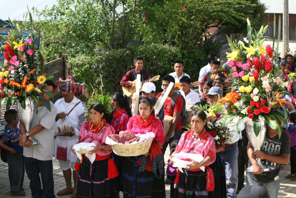 Color photograph of procession--men and children carrying large bouquets of flowers; three women, each carrying a basket.