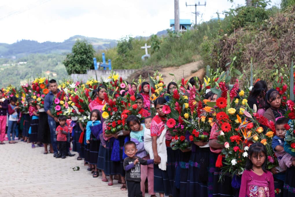 Color photograph of a large procession of men, women, and children carrying large bouquets of colorful flowers.