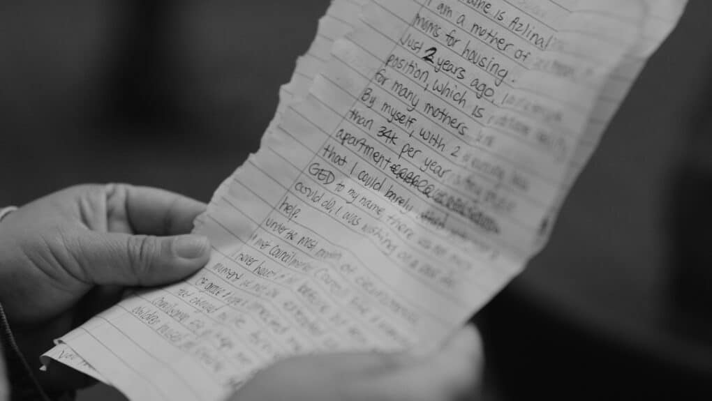 Black-and-white photograph of hands holding lined note-book paper pages with handwritten speech.