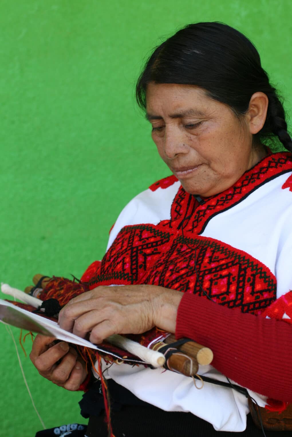 Color photograph of dark-haired middle-aged woman in red-and-white blouse, standing in front of a vivid green wall.