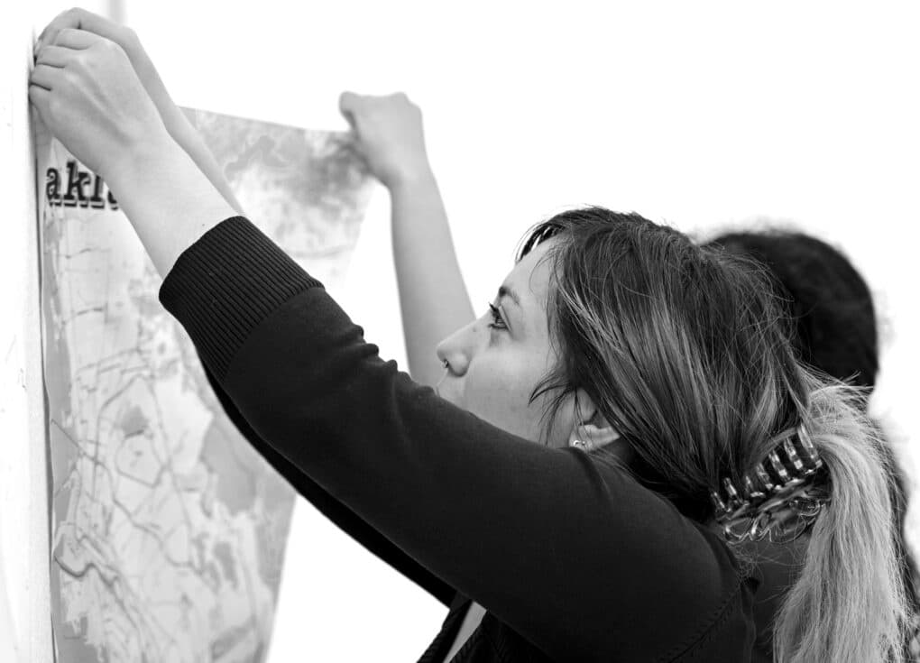 Black-and-white photograph of two young woman pinning up a map on a white wall.