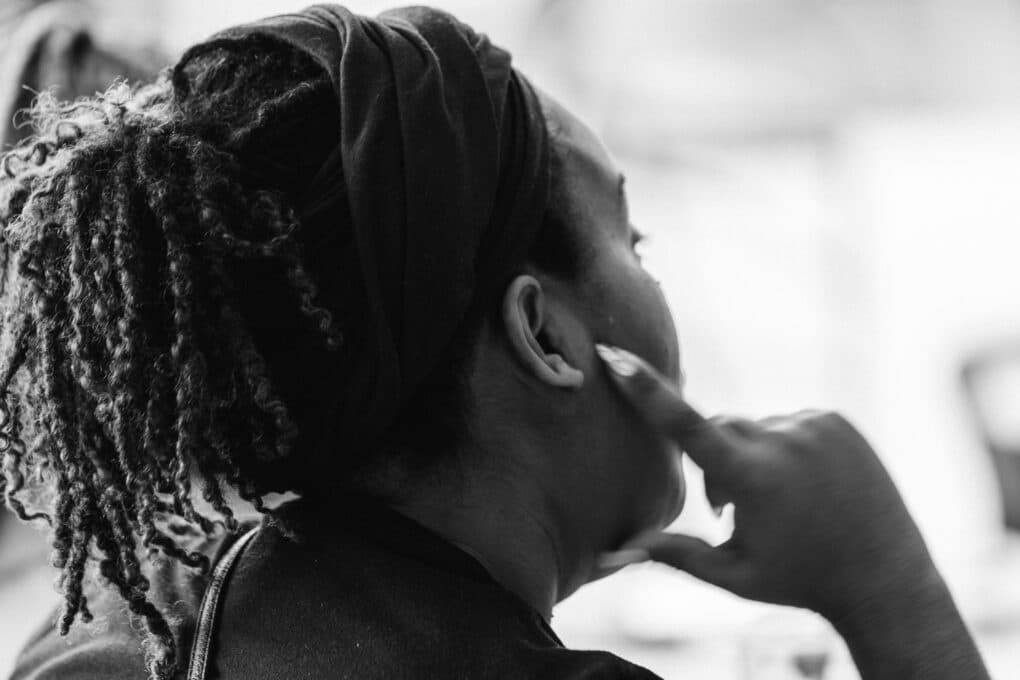 Black-and-white photograph of young Black woman, seen mostly from the back, with her hand to her cheek in a listening posture.