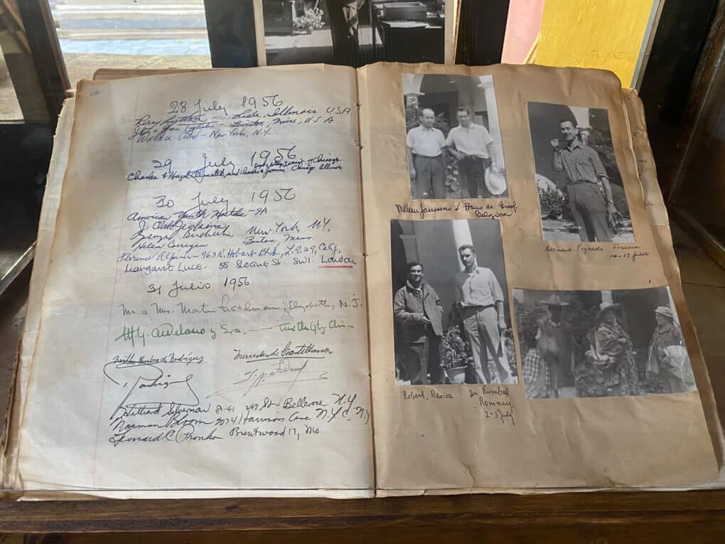 Color photograph of open ledger-style book with handwritten entries and pasted-in black-and-white photos of people.