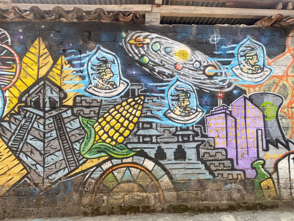 Color photograph of mural showing Aztec pyramids, ears of corn, and Aztec figures in spaceships.