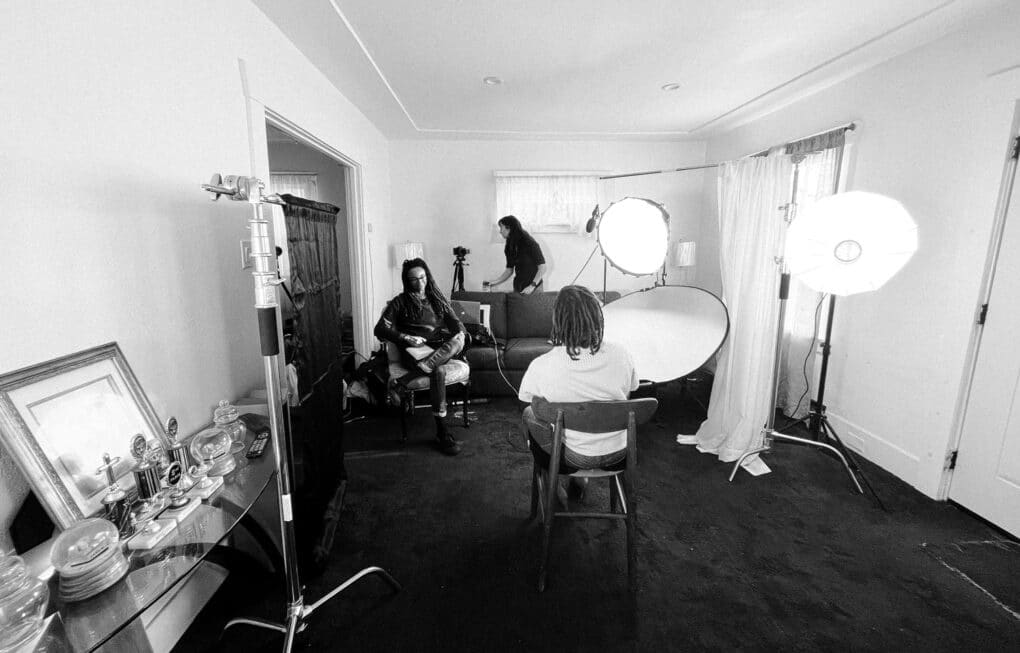 Black-and-white photograph of three people in a domestic interior, with large photographer's lights.