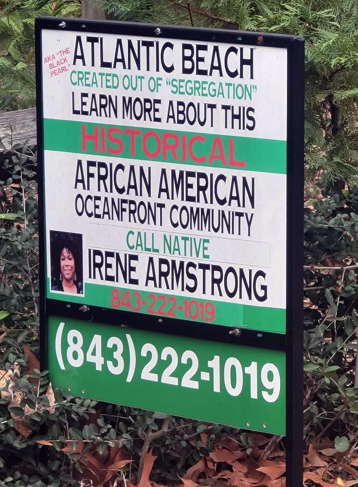 Color photograph of red, black, and green sign reading in part: "Atlantic Beach, created out of 'segregation.' Learn more about this historical African American oceanfront community."