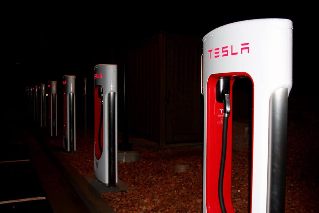 Color photograph of dramatically lit red-and-white Tesla charging stations, seen at night.