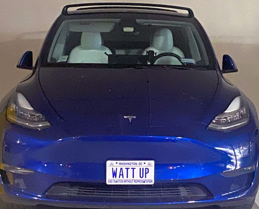 Color photogrpah of blue Tesla seen head on, with a Washington D.C. license plate reading WATT UP.