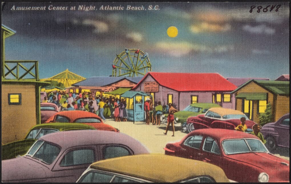 Colorized postcard of cars, bungalows, ferris wheel, and large crowd of Black beachgoers, under a full moon.