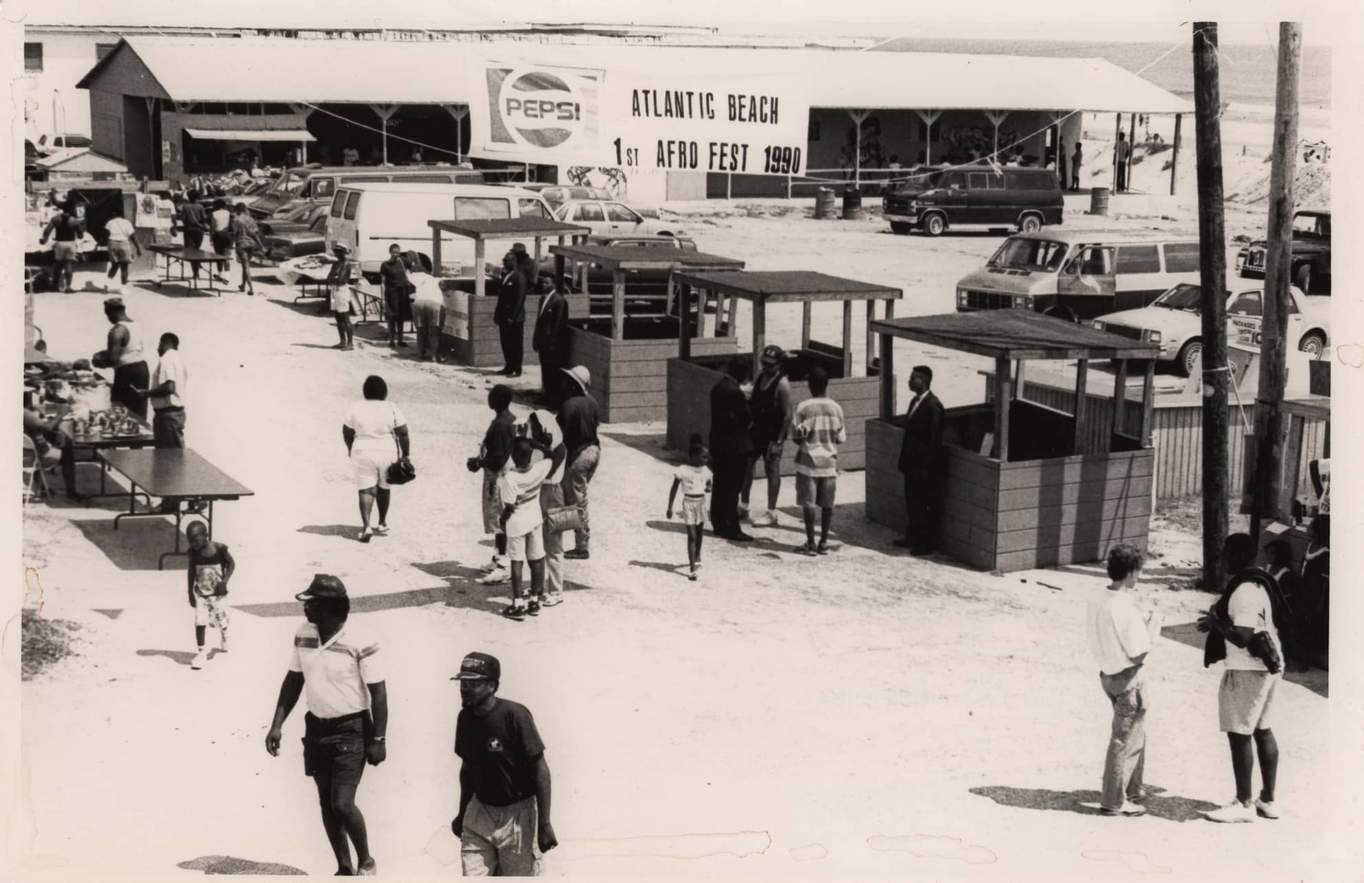 Click to Enlarge Black-and-white photograph of small crowd strolling beachside walkway.