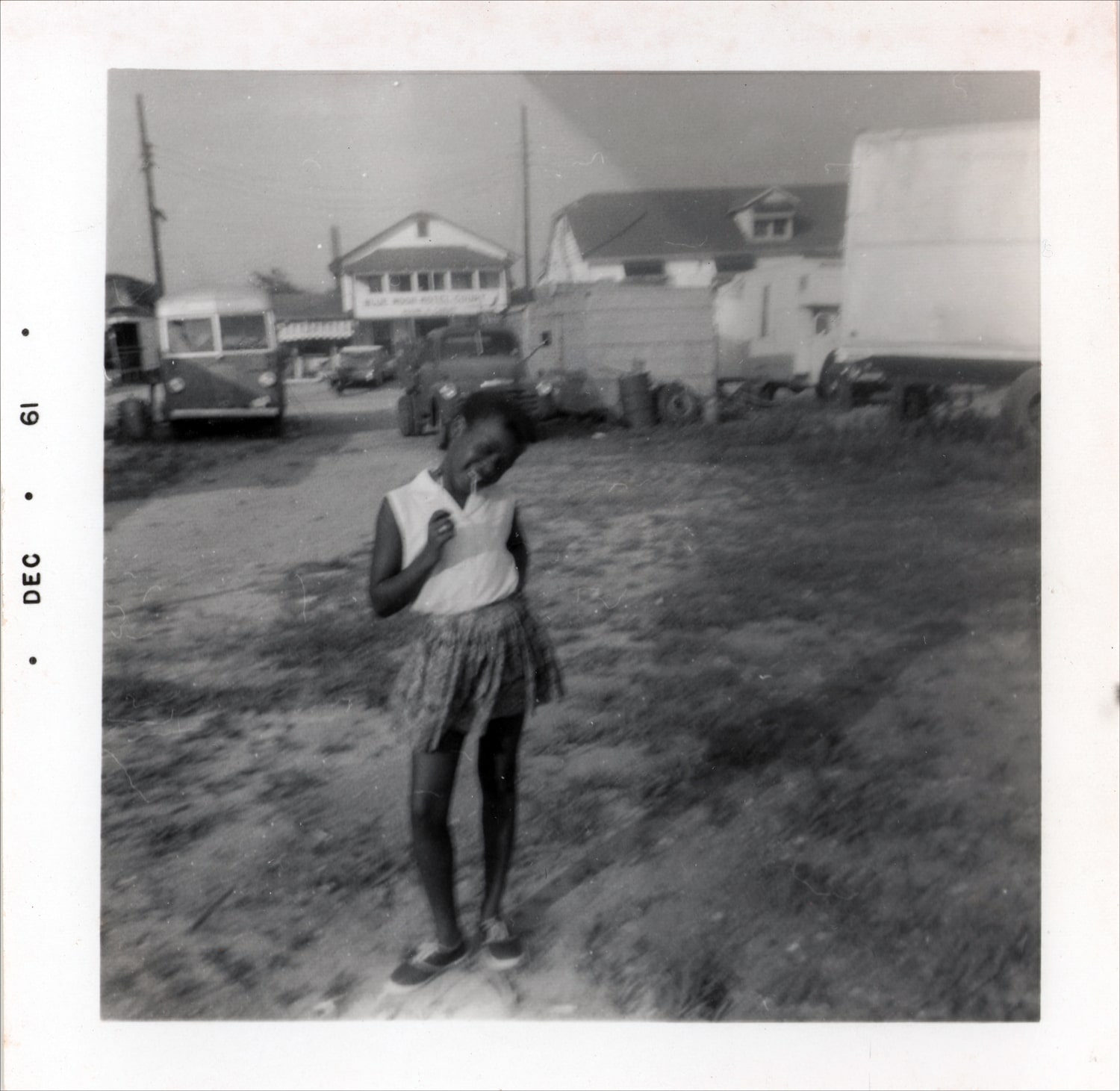 Click to Enlarge Black-and-white photo of young Black girl in a white sleeveless shirt, shorts, and sneakers.