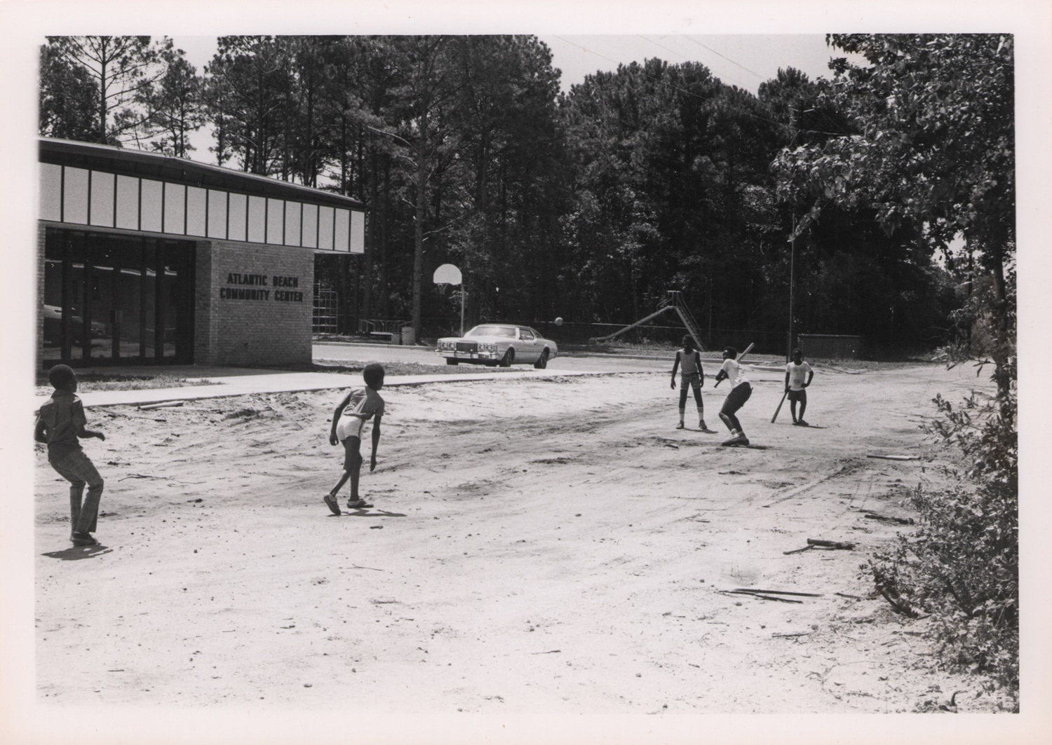 Click to Enlarge Black-and-white photograph of five Black boys playing a casual game of baseball in a sandy lot.