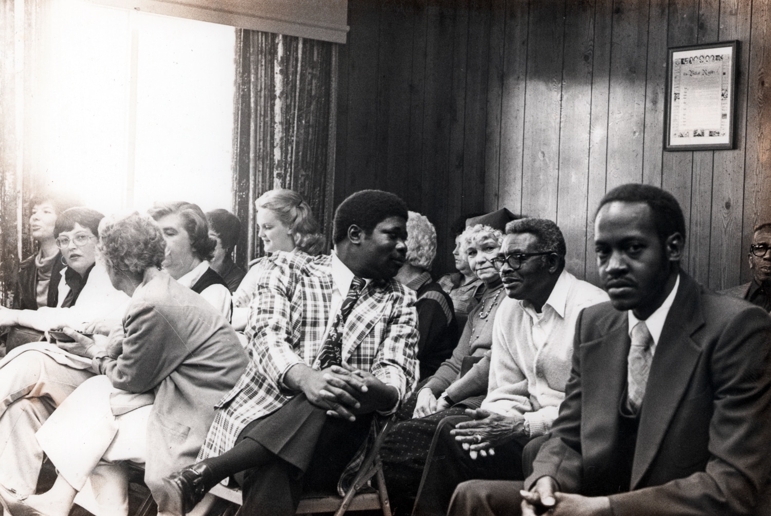 Click to Enlarge Black-and-white photo of Black and White well-dressed people seated in a wood paneled room.
