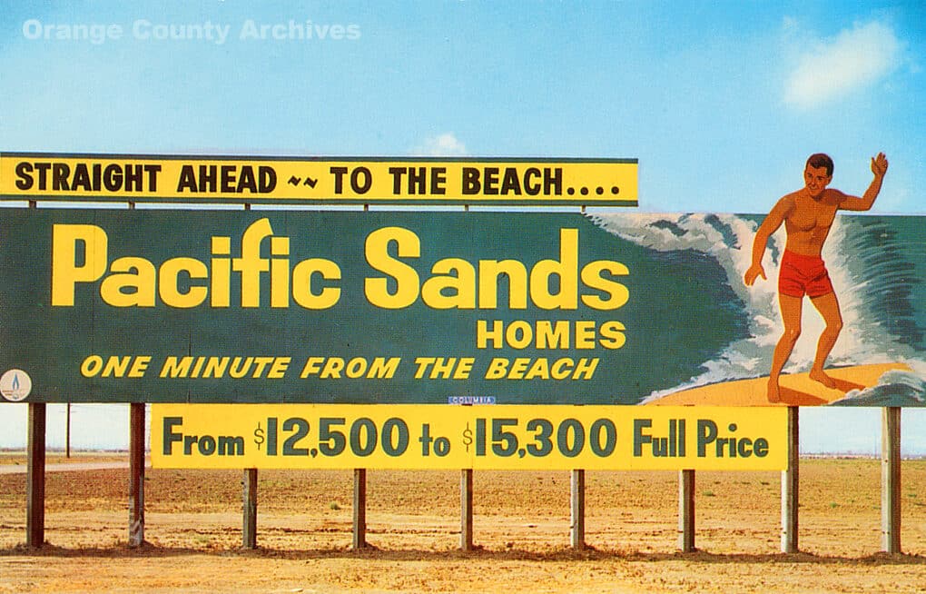 Brightly colored billboard on sand that advertises homes one minute away from the beach, and has a picture of a surfer. 