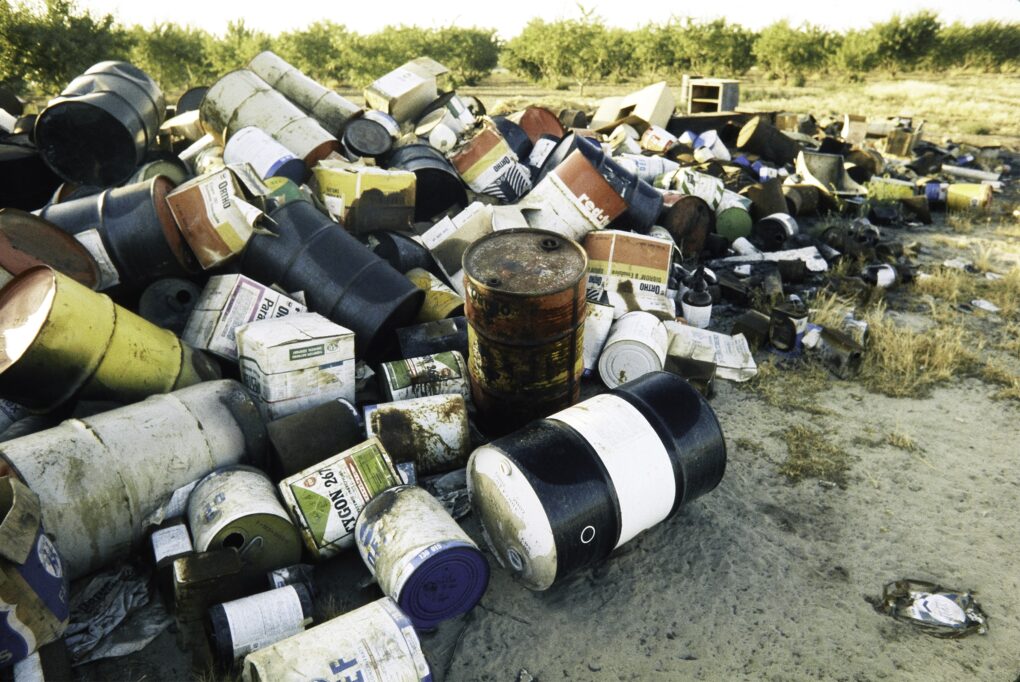 Large pile of dirty iron drums and gallon buckets, directly on the sand. 