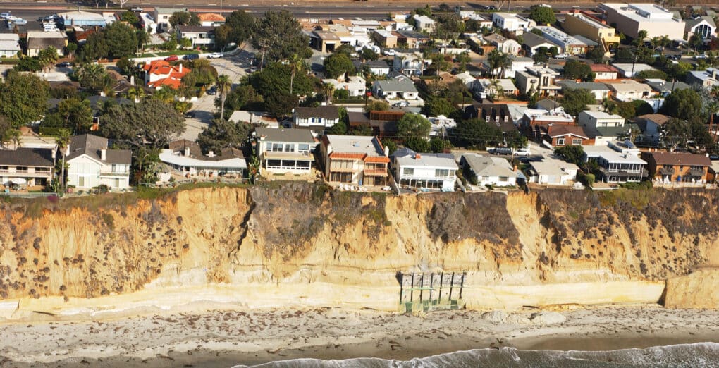 Aerial view of homes along a high sand bluff, with the ocean below. 