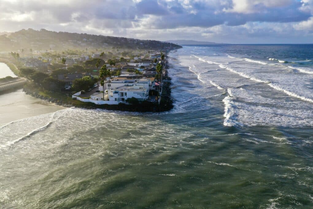 Aerial photo of a point surrounding on two sides by ocean, with densely situated large homes extremely close to the water. 