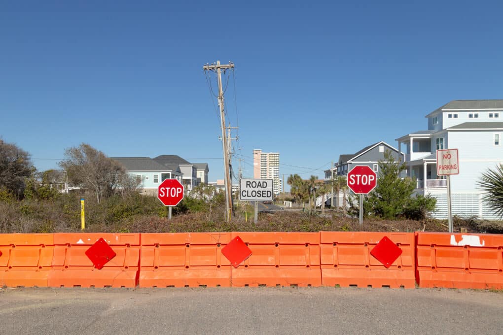 Color photograph of earthen barrier with stop signs, orange plastic barriers, and ROAD CLOSED sign.